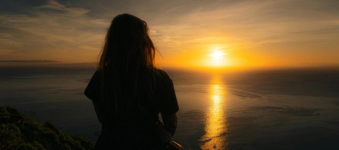 A woman sitting on a cliff watching the sunset