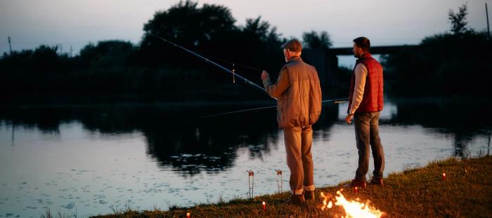 Rear view of senior man and son fishing at dusk in nature.