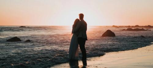 silhouette photo of couple standing on beach watching sunset