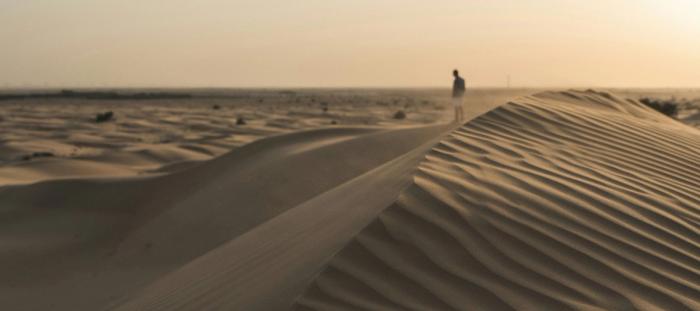 CC- a lone person stands on the backside of a sand dune as the wind blows sand around their legs