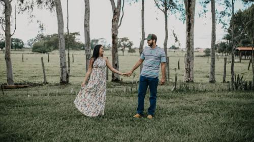 A man and woman holding hands while standing on a lawn bordered by trees.