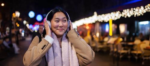 A woman wearing headphones walking down a festively-lit steet