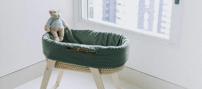A green crib with a teddy bear inside it in a white room
