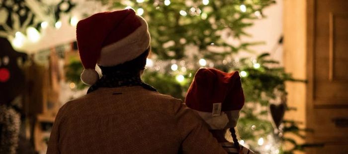 Adult in Santa hat, hugging little girl in santa hat, admiring lit tree