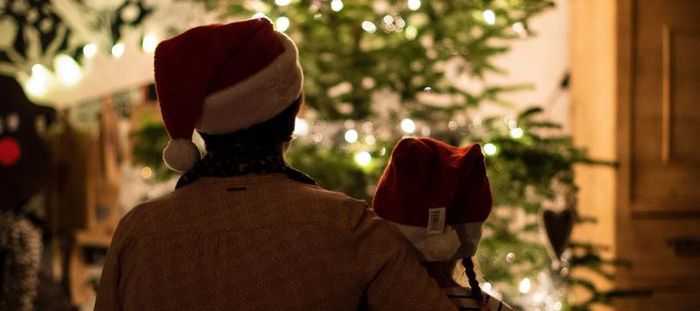 Adult in Santa hat, hugging little girl in santa hat, admiring lit tree