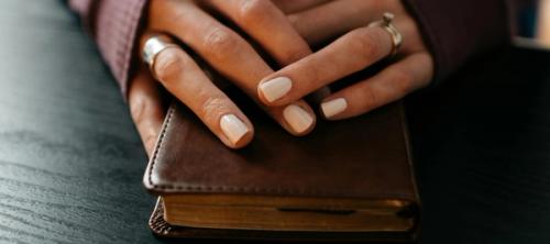 A woman's folded hands resting on a small leather Bible.