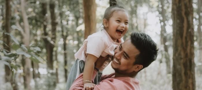 a person lifting up child lauging in woods