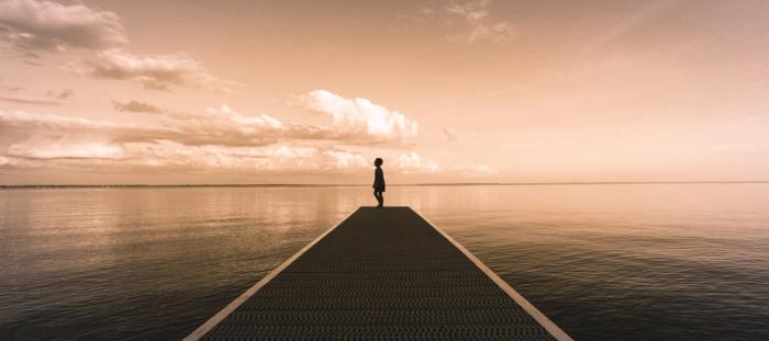 boy standing on edge of doc overlooking the ocean at sunset