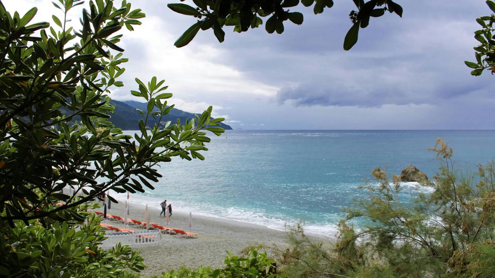 Spiaggia di Monterosso al Mare in una giornata nuvolosa, con il mare, gli ombrelloni e il lungomare delle Cinque Terre avvolti da un'atmosfera tranquilla.