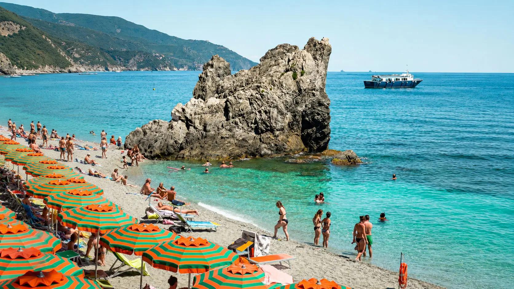 Spiaggia di Monterosso al Mare con la celebre roccia che emerge dal mare, acqua cristallina e panorama della costa delle Cinque Terre.