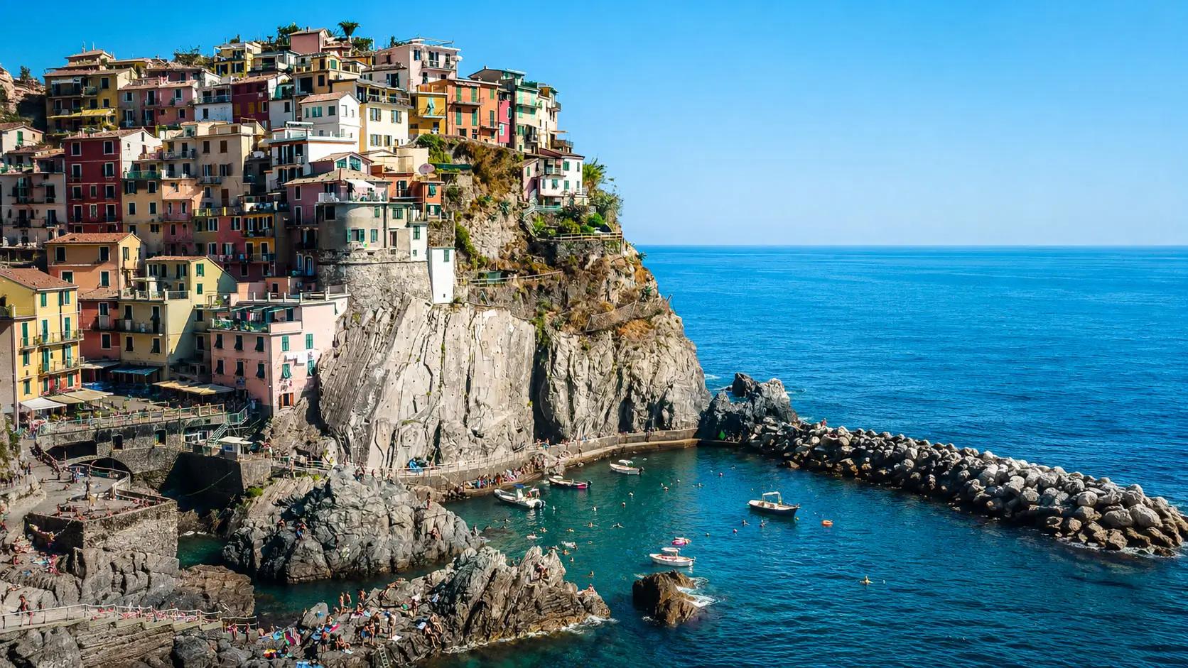 La celebre vista di Manarola, con le luci calde dei lampioni e delle case colorate che si accendono sullo sperone di roccia scura, specchiandosi nel mare blu cobalto.