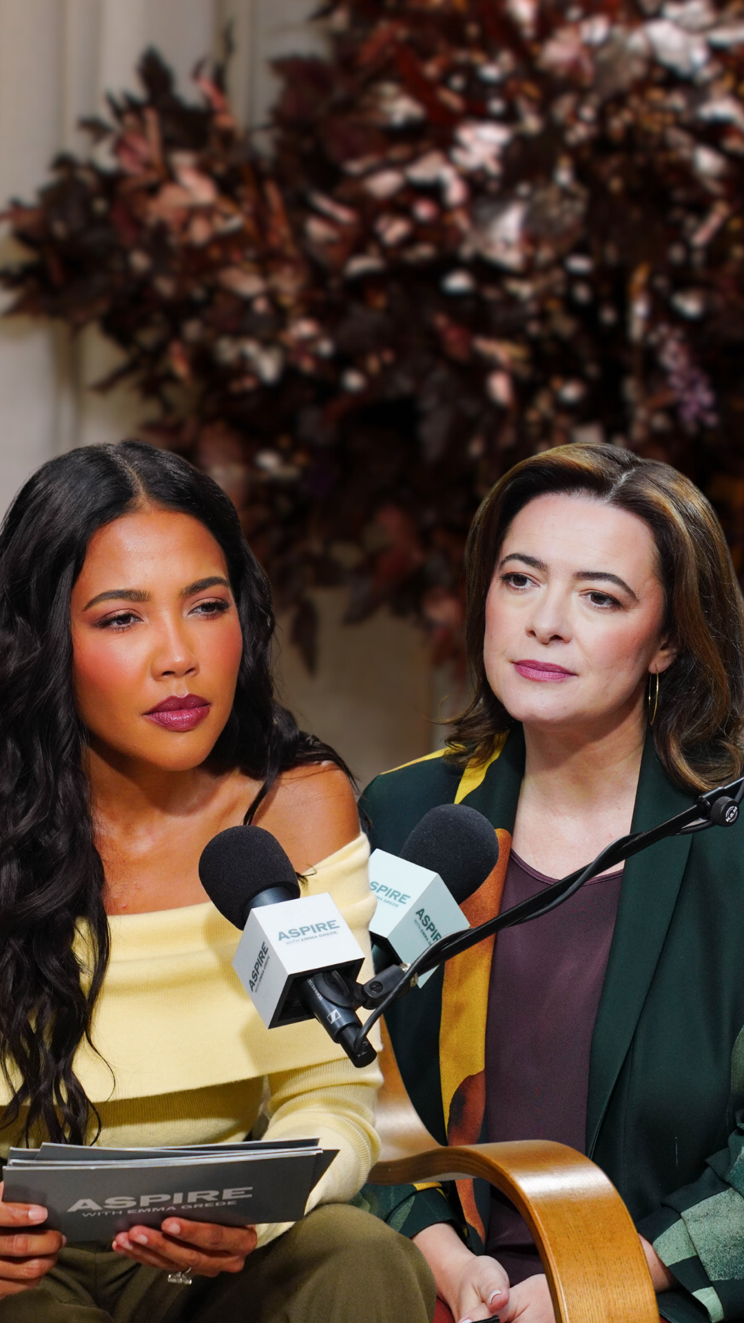 Two women, one in a yellow top and one in a green blazer, seated with "ASPIRE" microphones for a podcast or interview. The woman on the left holds an "ASPIRE" booklet.