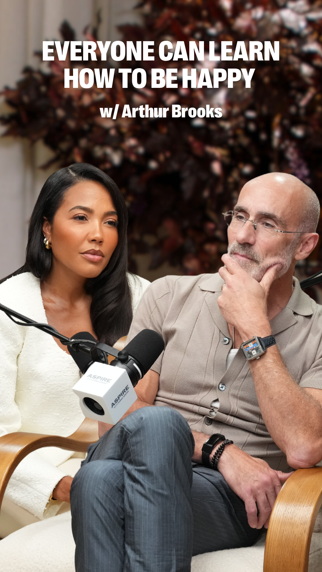 A woman and a man talk into microphones in a podcast setting. Text overlay: "EVERYONE CAN LEARN HOW TO BE HAPPY w/ Arthur Brooks."