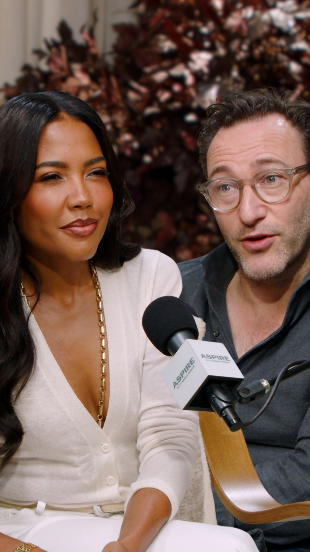 A woman Emma Grede in a white top and a man Simon Sinek in glasses speak into an Aspire branded microphone.