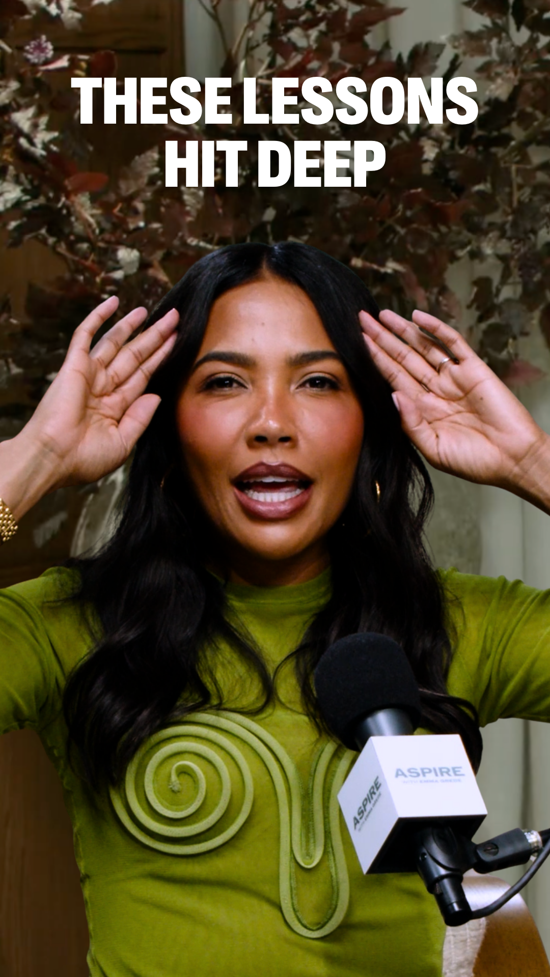 A woman emma grede, wearing a lime green top with a spiral design, gestures with her hands while speaking into an Aspire microphone. White text above reads "THESE LESSONS HIT DEEP".