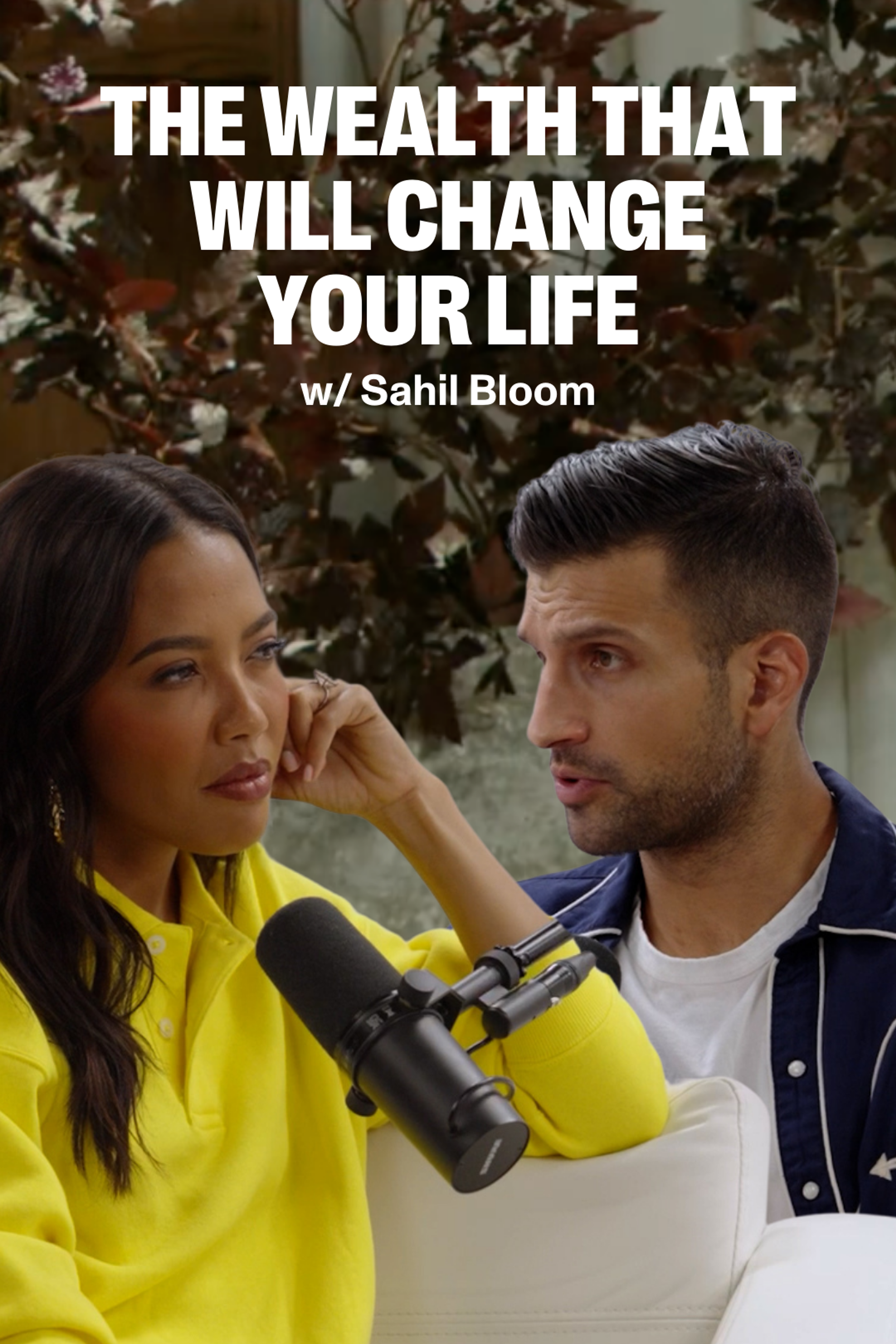 Emma Grede in a yellow top listens to a man speaking, with a microphone between them. Overlay text reads "THE WEALTH THAT WILL CHANGE YOUR LIFE w/ Sahil Bloom".