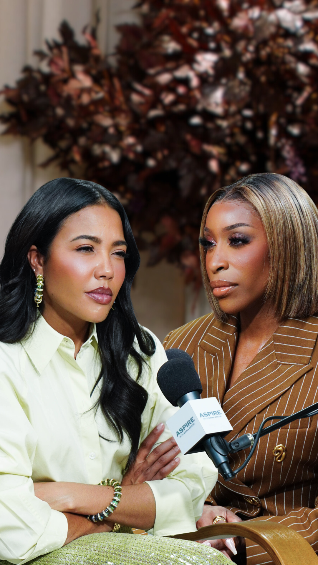 Two women are seated for an interview with an Aspire microphone between them. The woman on the left has long dark hair and a light green shirt, while the woman on the right has blonde-streaked hair and a brown pinstripe blazer.