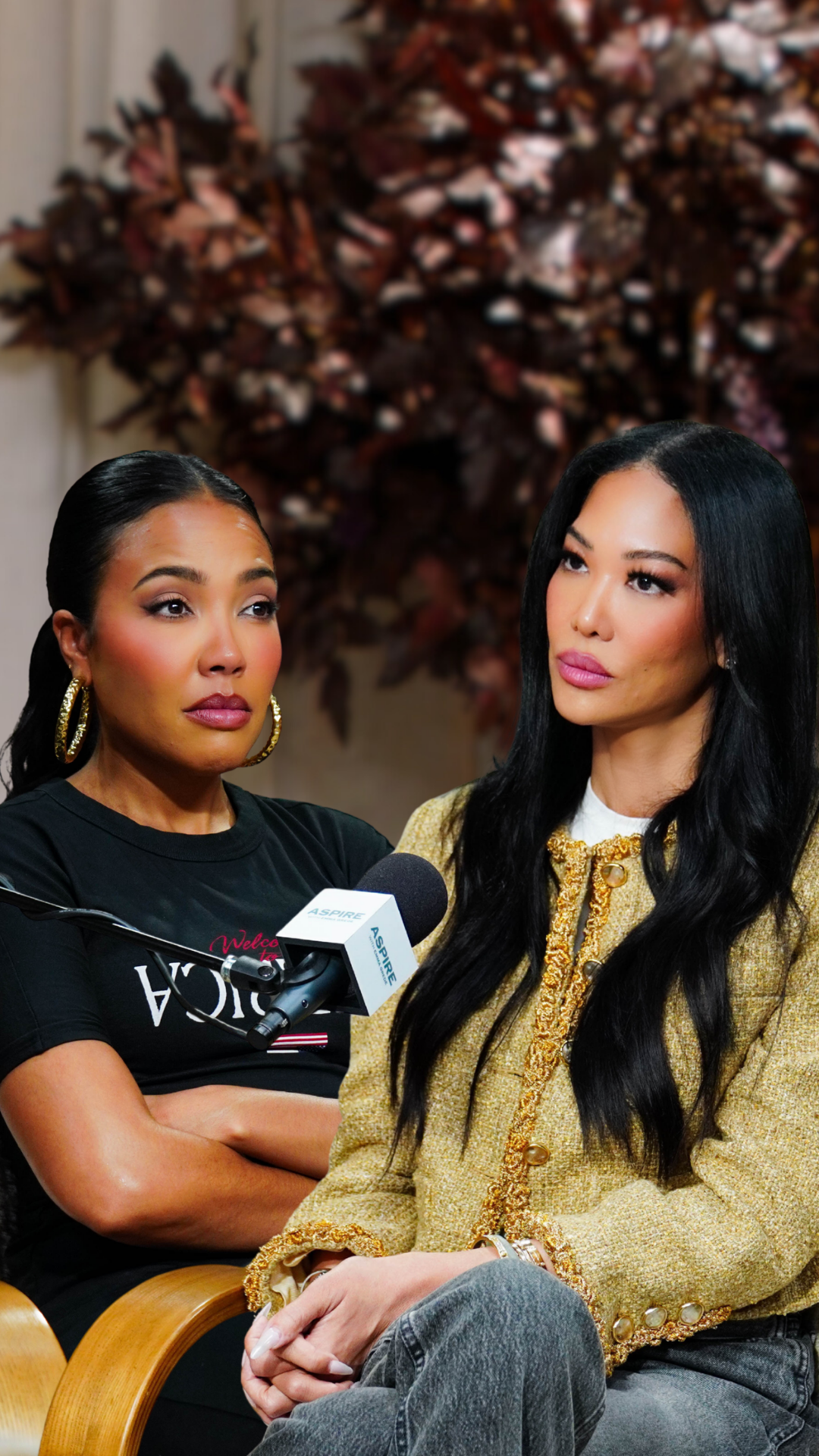 Two women, one in a gold tweed jacket and one in a black t-shirt, sit with a microphone between them during an interview.