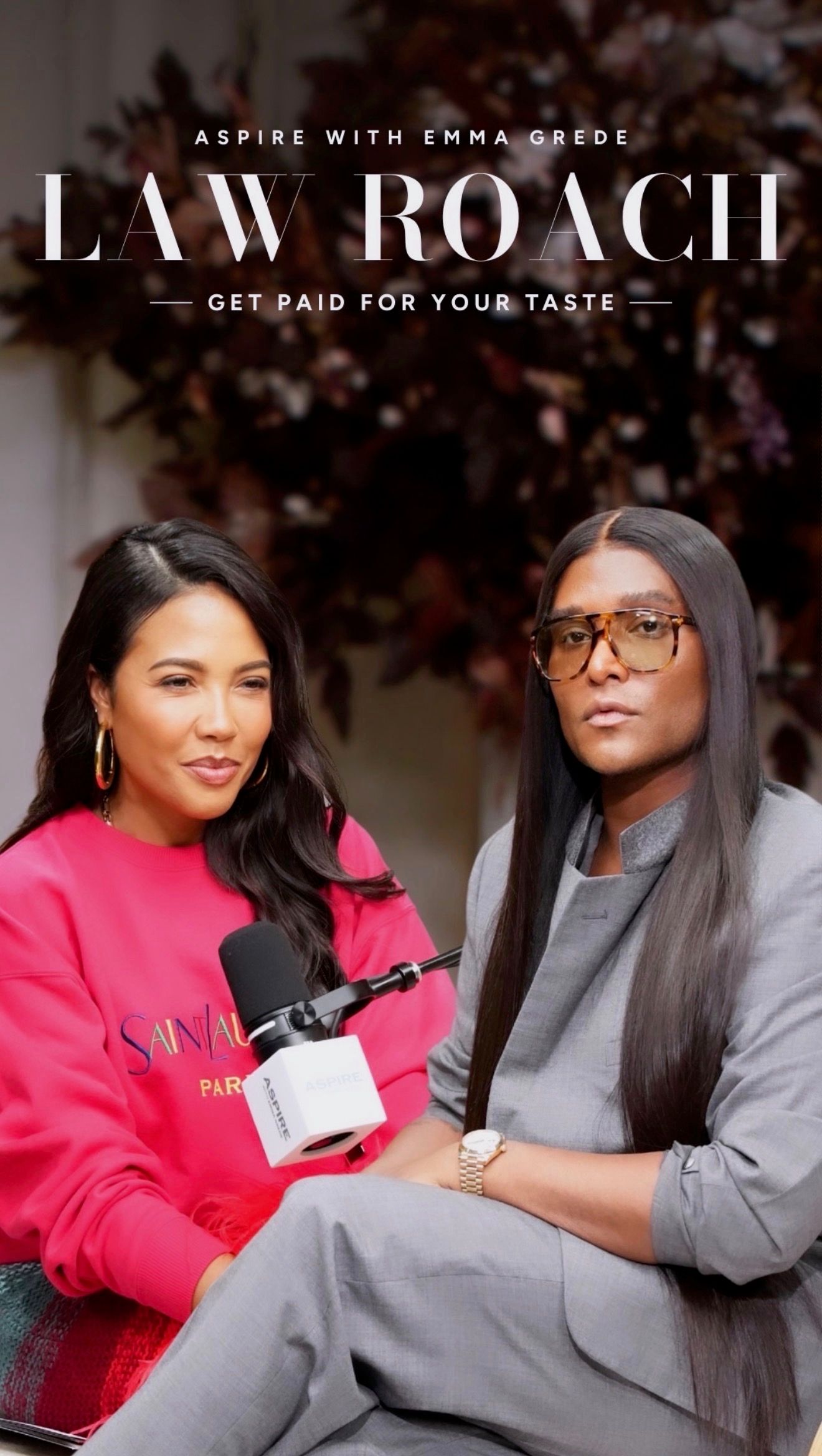 Emma Grede in a pink sweatshirt and Law Roach in a grey suit and glasses are seated for a podcast, with the title "ASPIRE WITH EMMA GREDE LAW ROACH GET PAID FOR YOUR TASTE" displayed above.