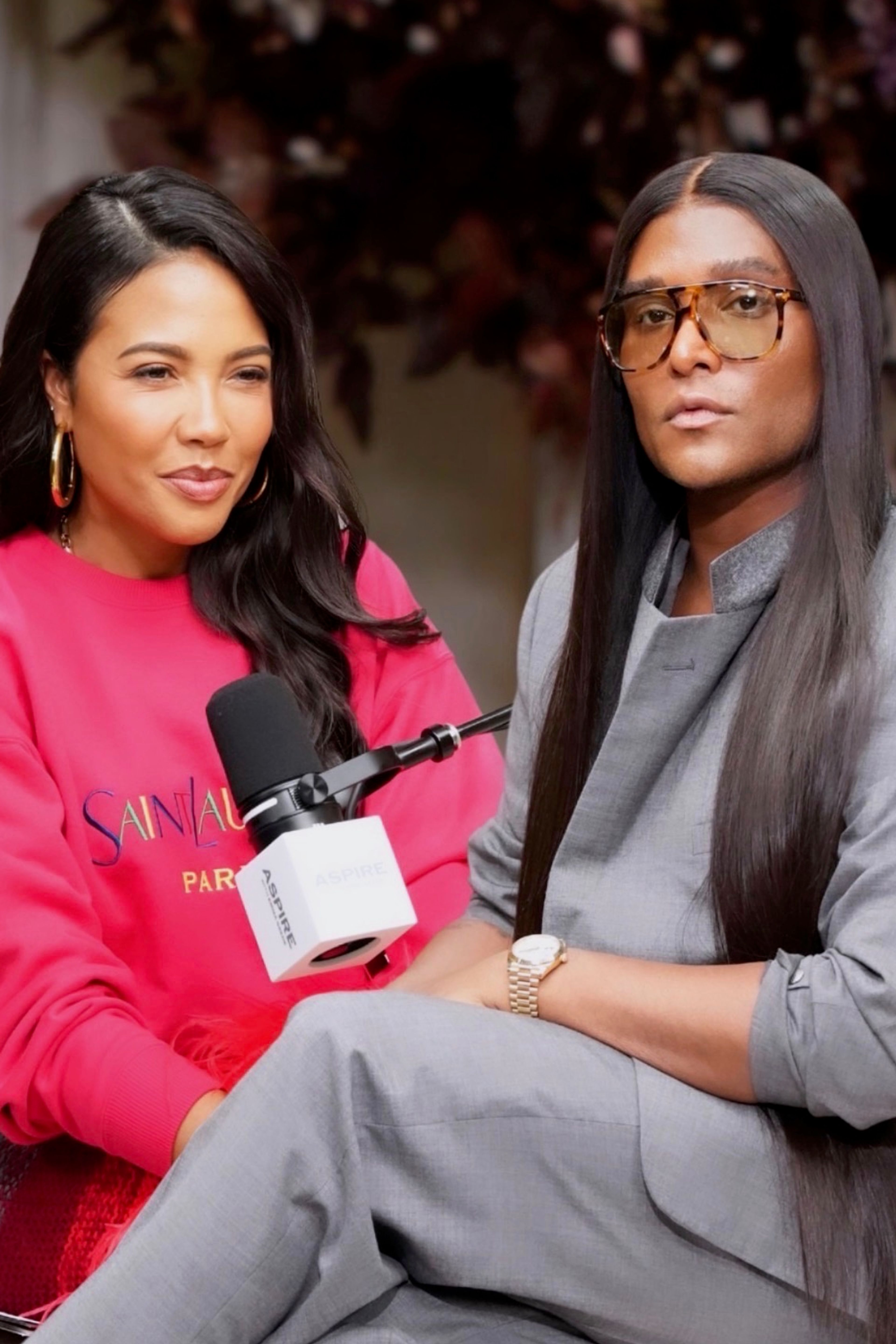 Emma Grede in a pink sweatshirt and Law Roach in a grey suit and glasses are seated for a podcast, with the title "ASPIRE WITH EMMA GREDE LAW ROACH GET PAID FOR YOUR TASTE" displayed above.