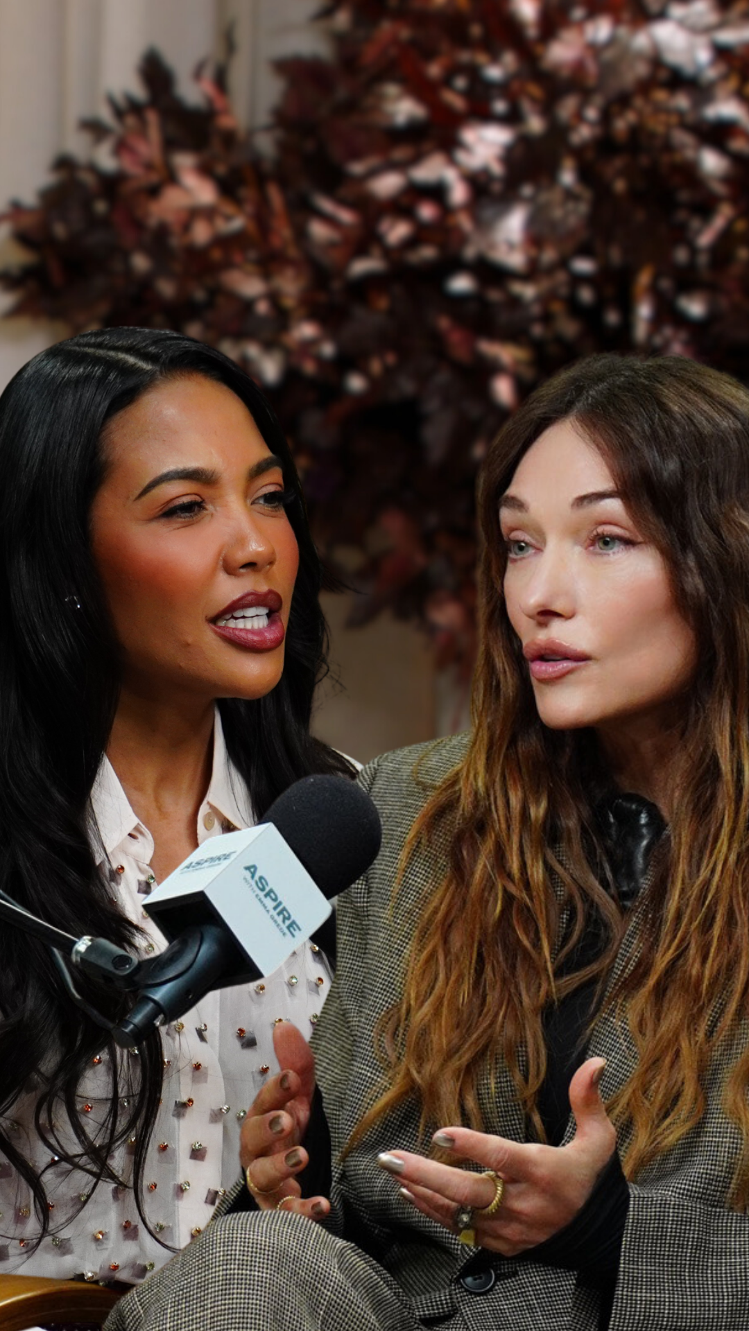 Two women, one speaking into a microphone and the other gesturing, engaged in conversation.