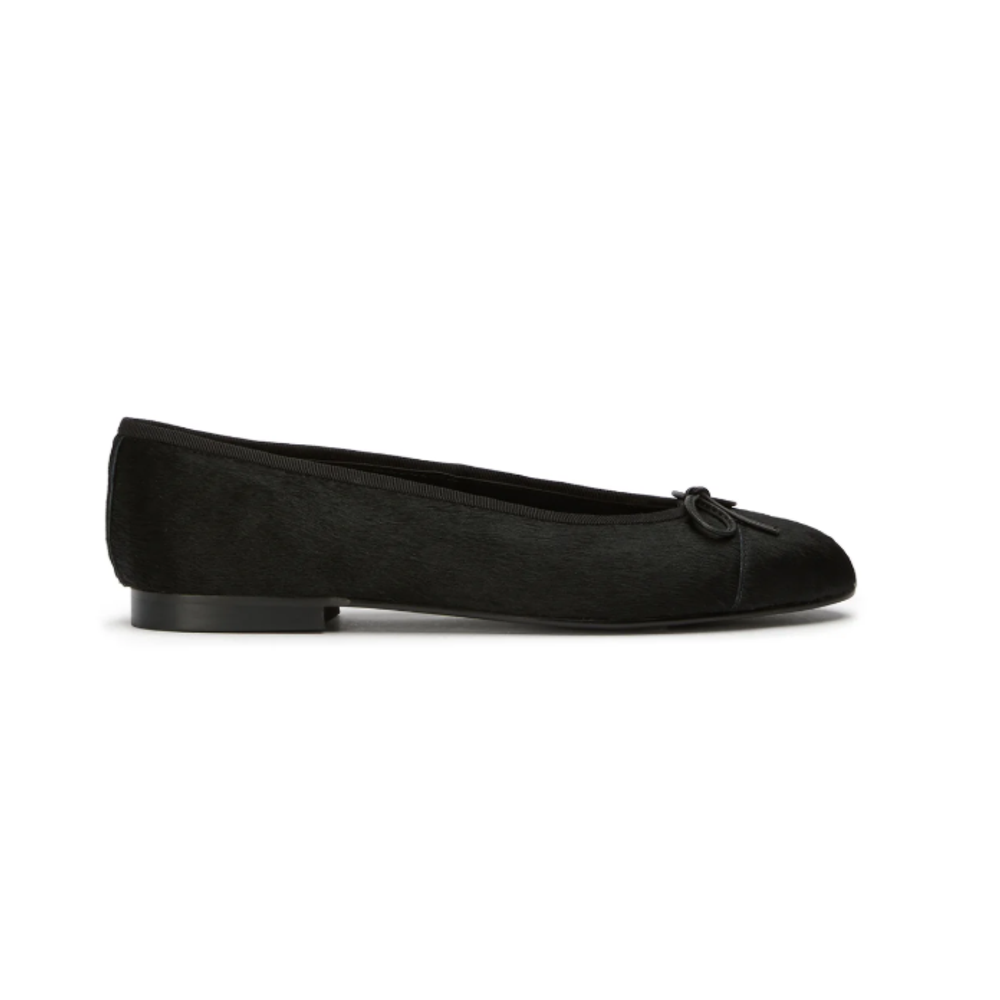 Tony Bianco Robyn ballet flat in black pony hair, featuring a round cap toe, a delicate leather bow detail, and a low 1cm heel against a white background.