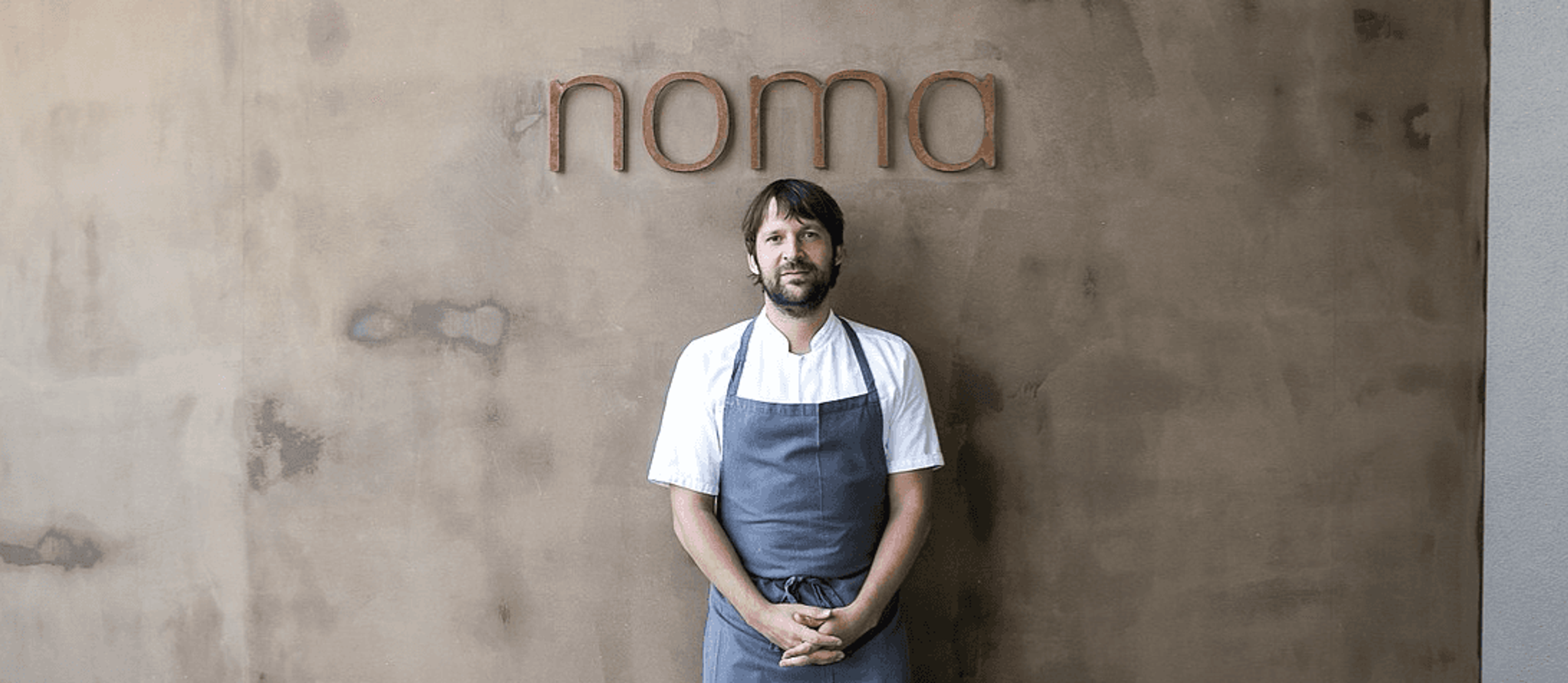 Head chef standing in front of the Noma wordmark on a textured wall