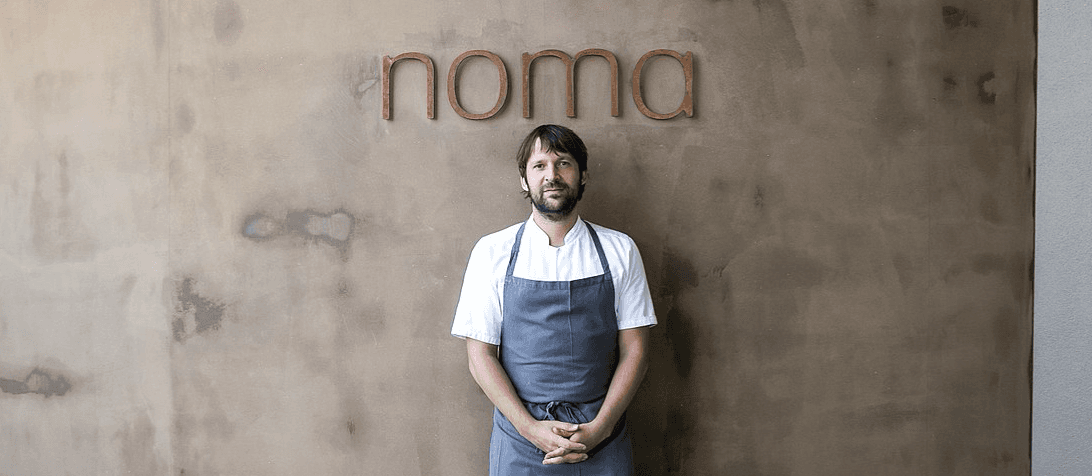 Head chef standing in front of the Noma wordmark on a textured wall