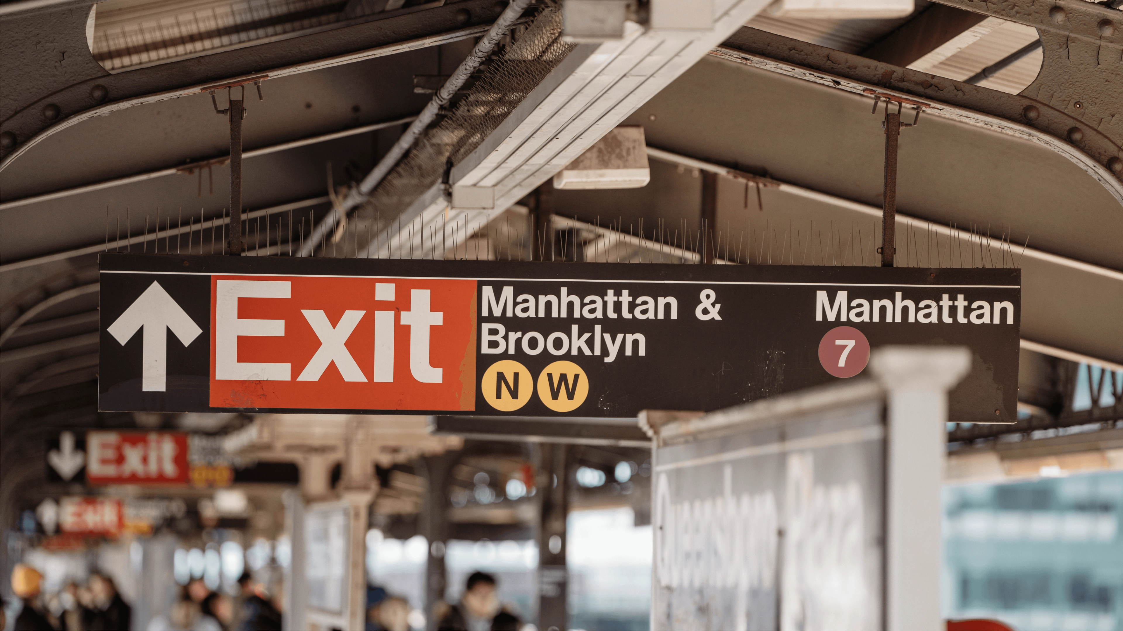 New York City subway exit sign showing Helvetica-style typography with directional arrows and colored line symbols.