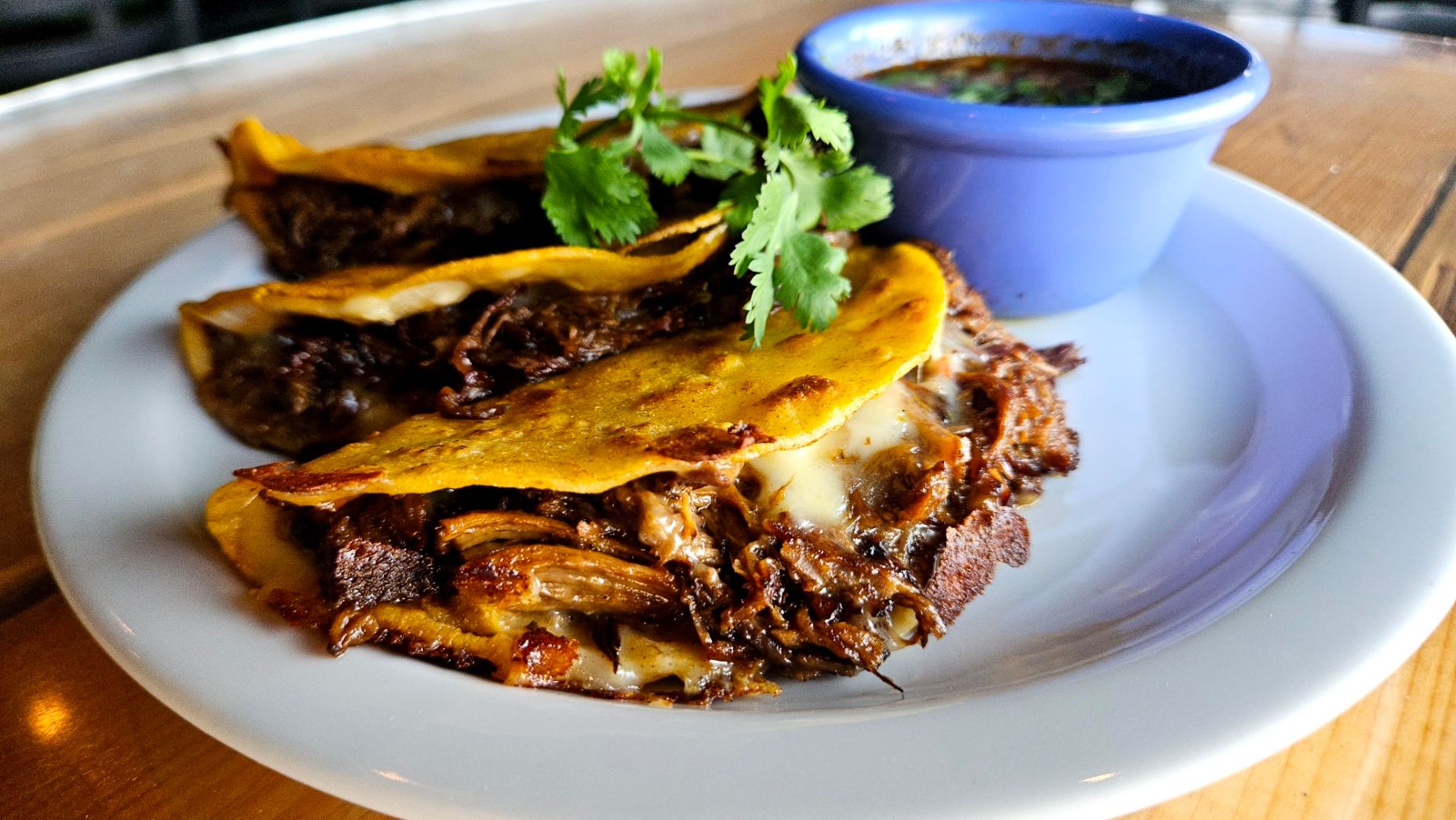 Birria tacos with melted cheese, cilantro and a cup of consommé