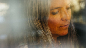 Soft, close-up portrait of a woman with long hair looking down thoughtfully, captured through a hazy, light-filled foreground.