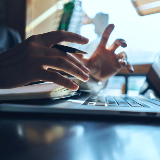 Person sitzt vor einem Laptop. Fokus ist auf den Fingern.