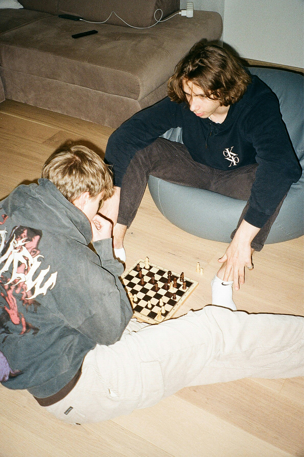 Två unga män spelar schack på ett trägolv