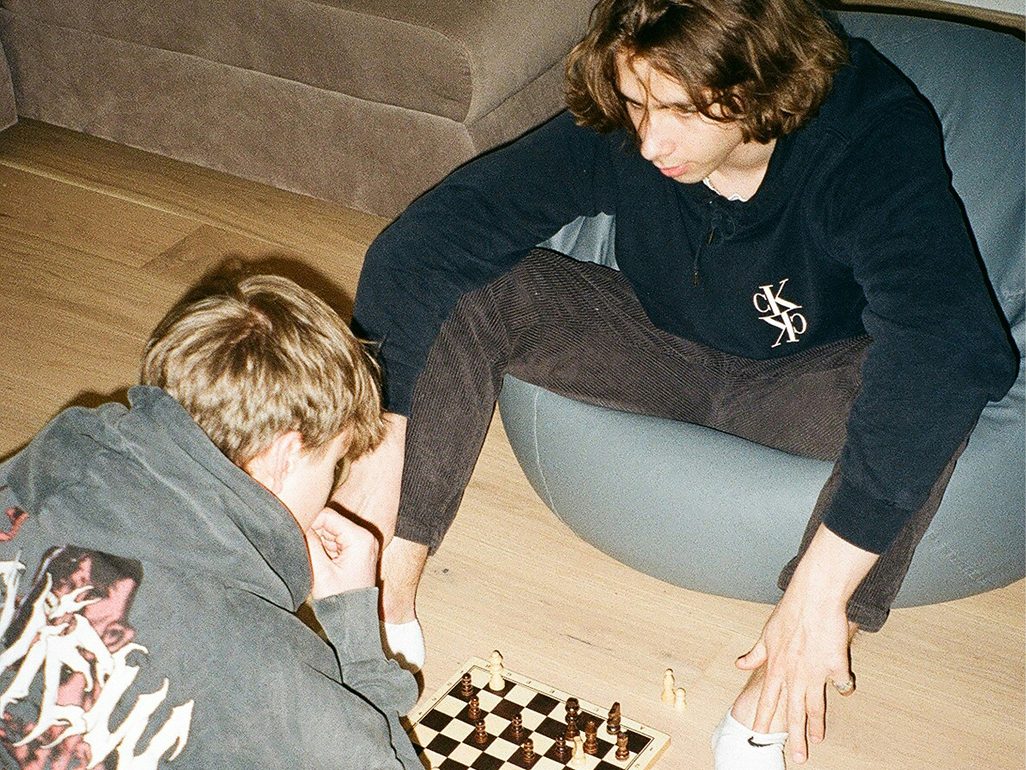 Två unga män spelar schack på ett trägolv