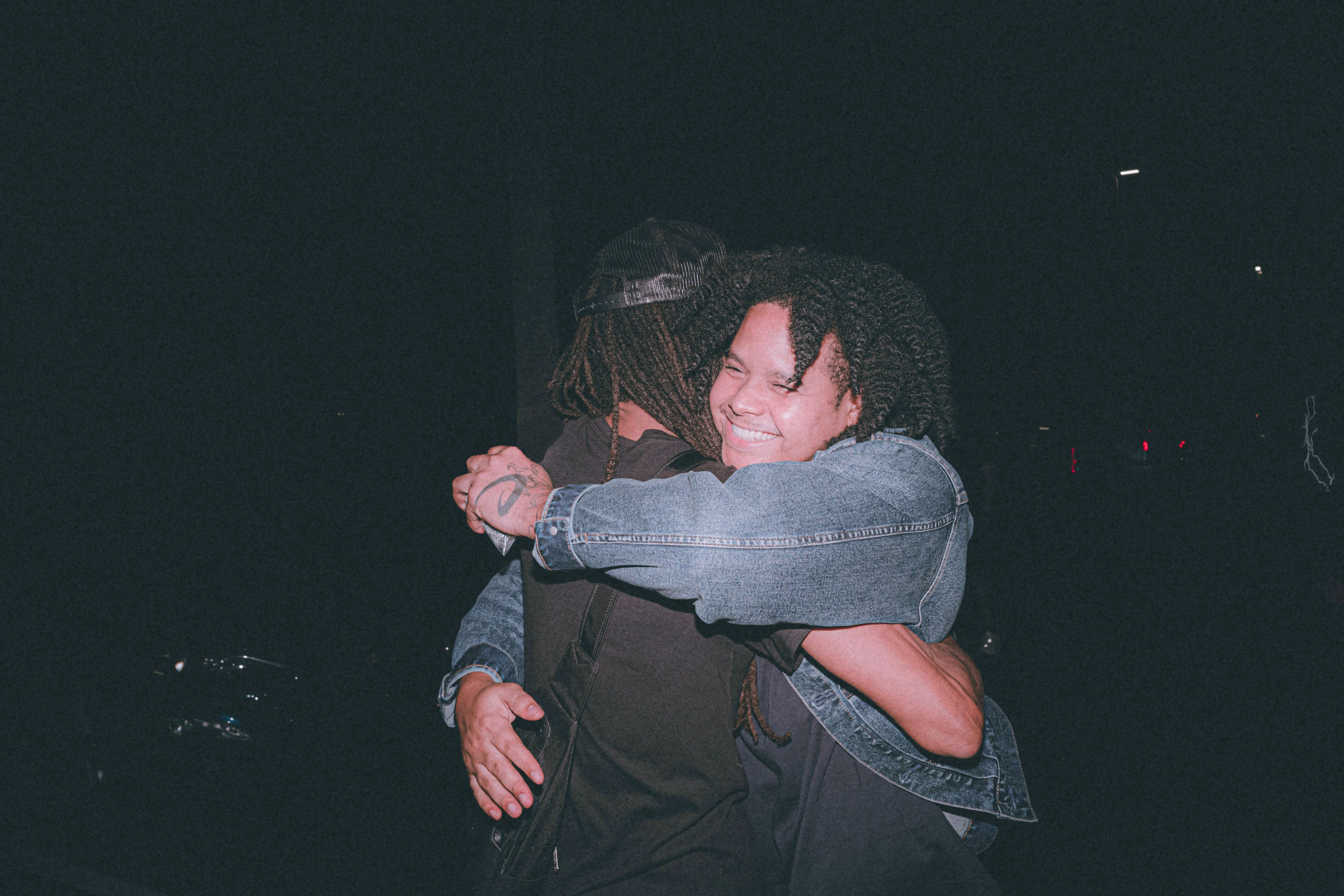 Två personer som kramas i mörkret; den ena ler brett.