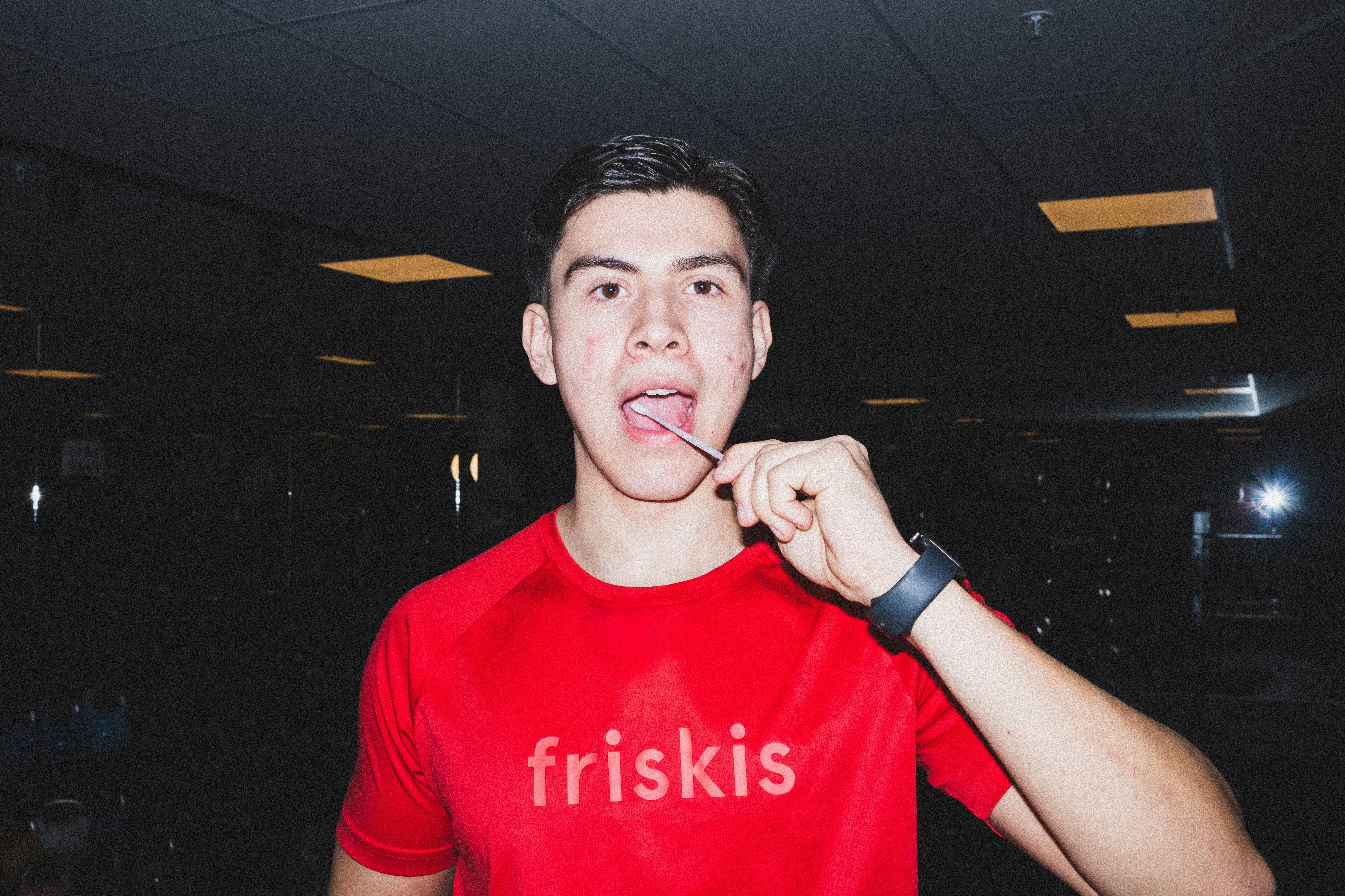 En ung man i en röd "friskis"-tröja håller en klubba mot tungan och tittar in i kameran.