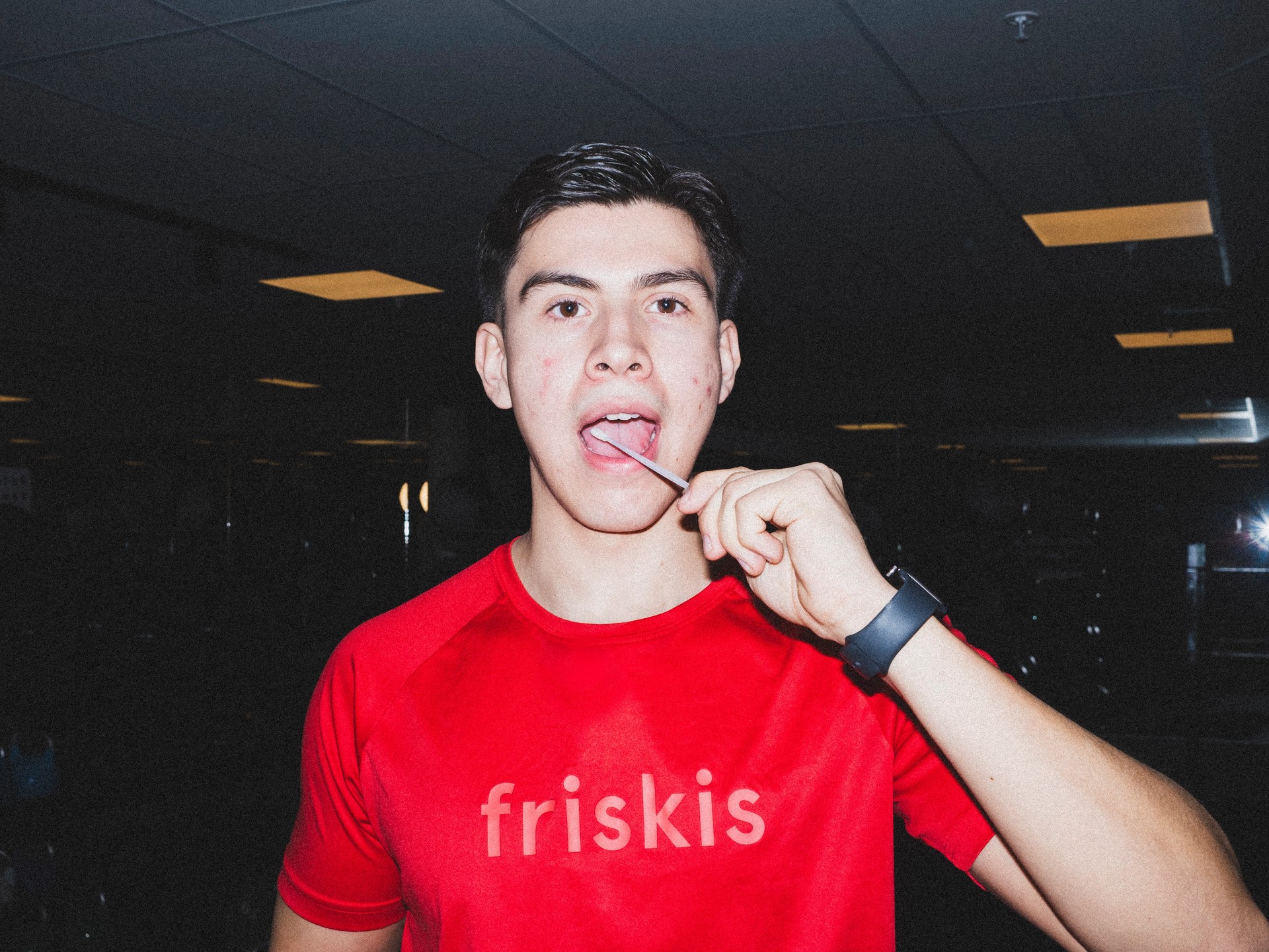 En ung man i en röd "friskis"-tröja håller en klubba mot tungan och tittar in i kameran.