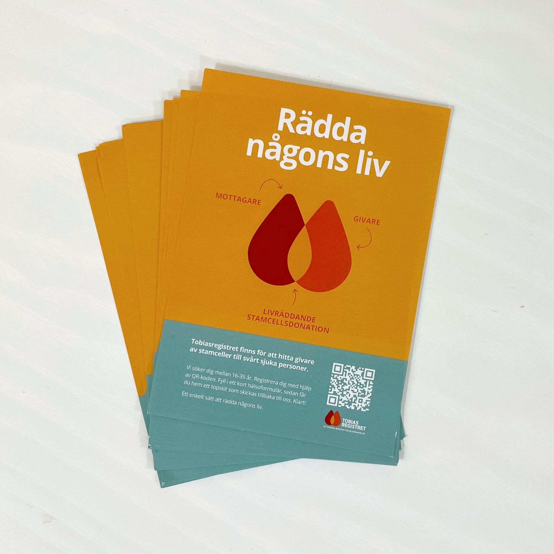 A stack of orange and teal brochures promoting stem cell donation, featuring interconnected blood-like drops and the Swedish text "Rädda någons liv" (Save someone's life).