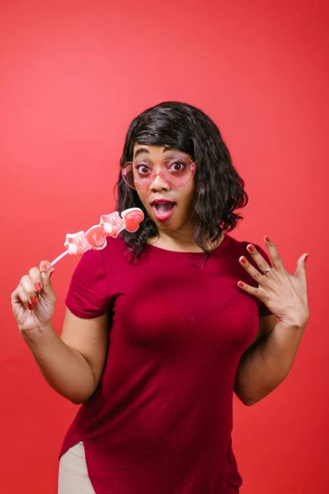 : A surprised woman wearing pink heart-shaped glasses and holding heart candies, symbolizing the realization that relying on casual, 20s-era dating rules no longer works in your 30s.