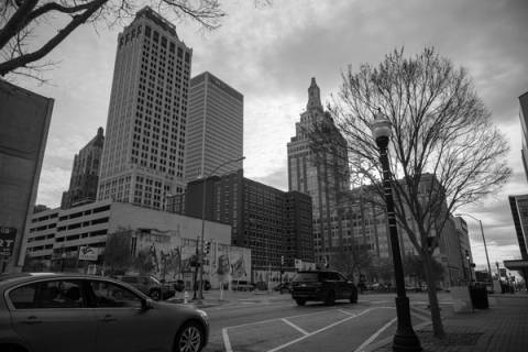 A black and white photograph of historic downtown Tulsa architecture, including a parking garage and skyline, representing the walkable districts like Blue Dome and Brady Arts discussed in the Beyond The Sparks guide.
