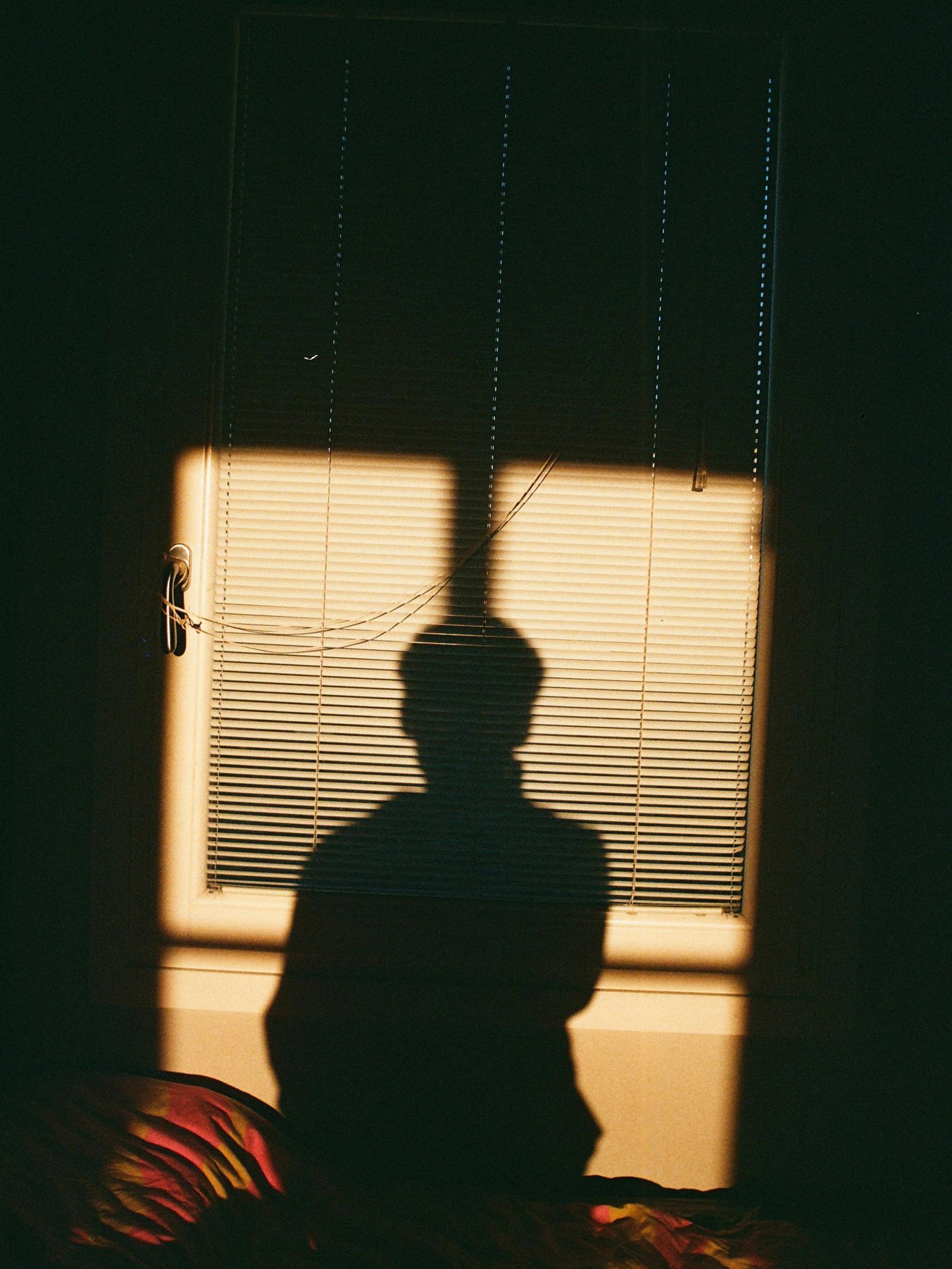 The soft silhouette of a person near a window, turned toward the light.