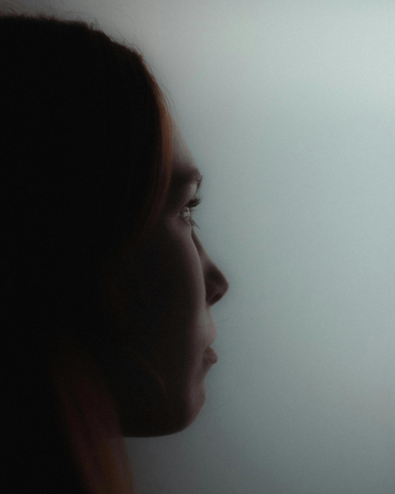 A close profile of a person looking down in soft, low light.