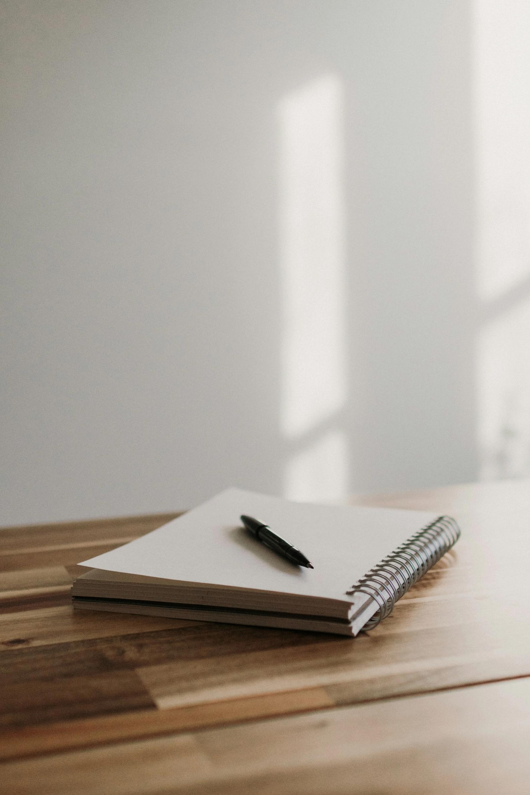 A blank notebook and pen on a wooden table in soft light.