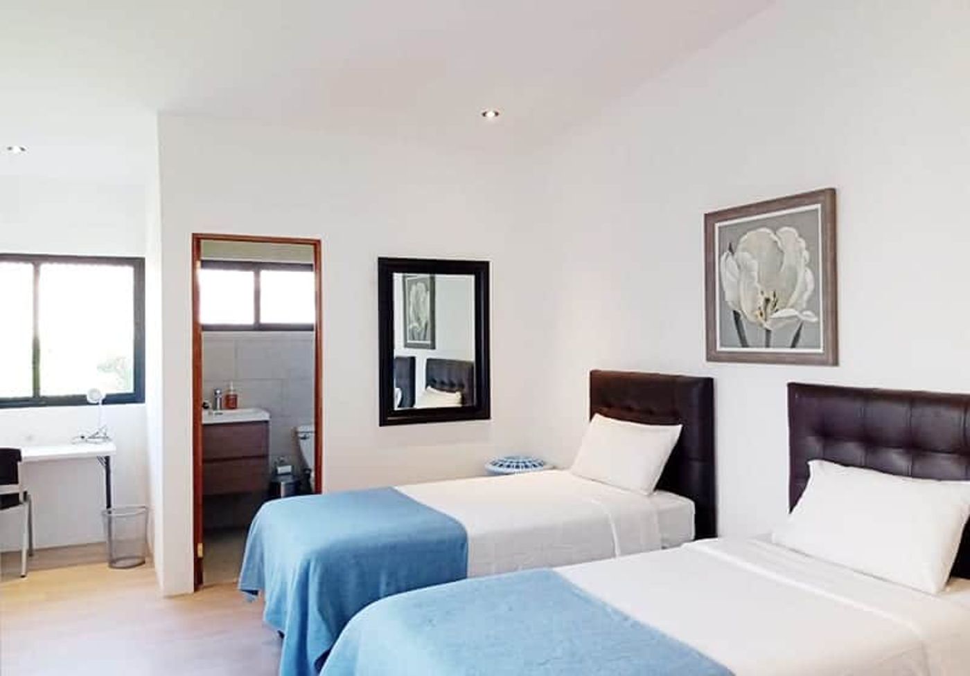 Shared room at the San José residence with twin beds, white linens and a soft-blue throw, and an open bathroom doorway.