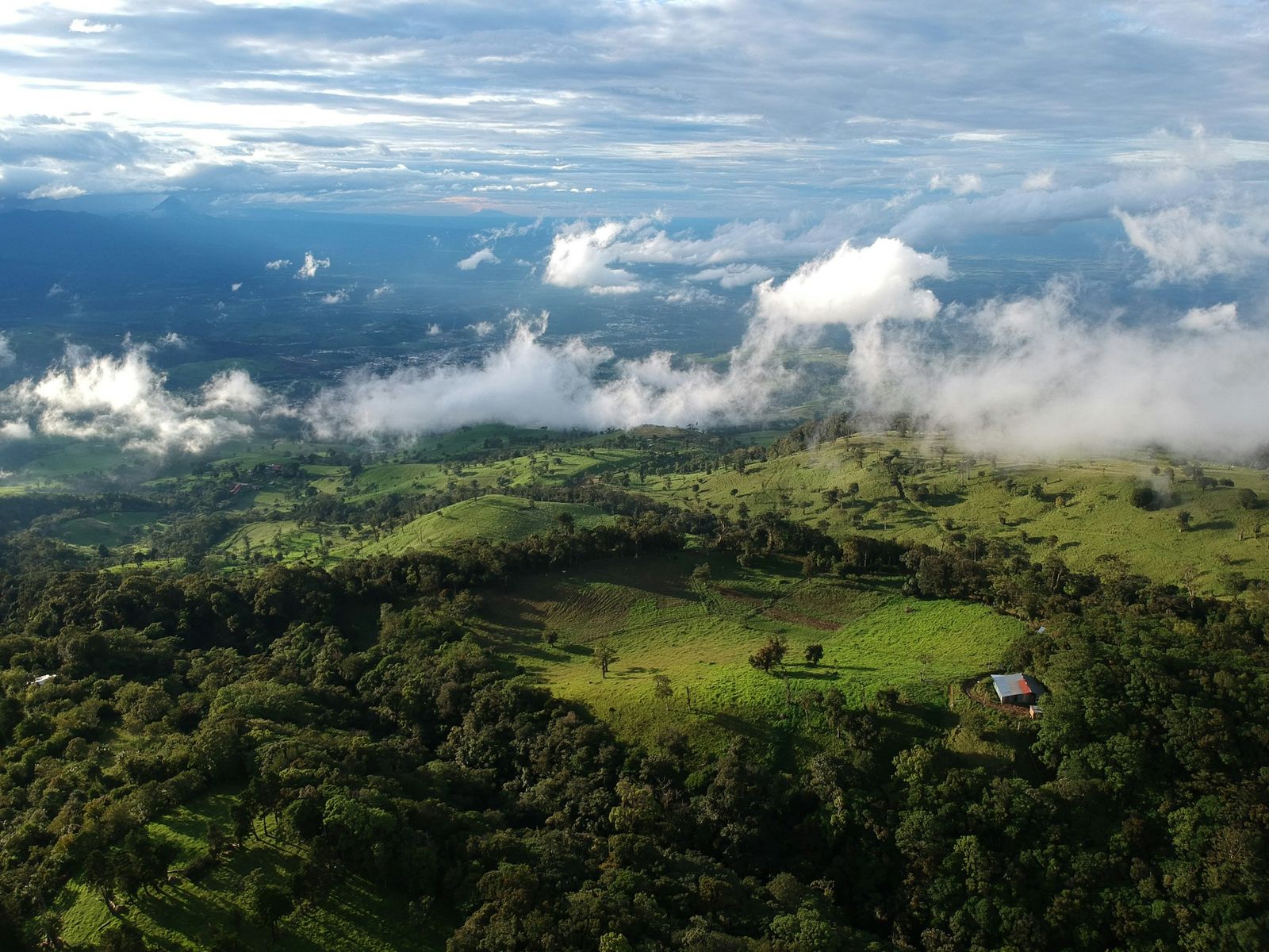 An aerial view of green hills and low clouds over a wide valley.