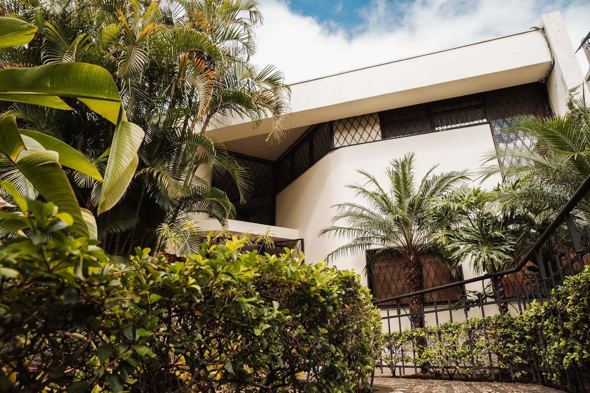 The white San José residence among palms and tropical plants under a blue sky.