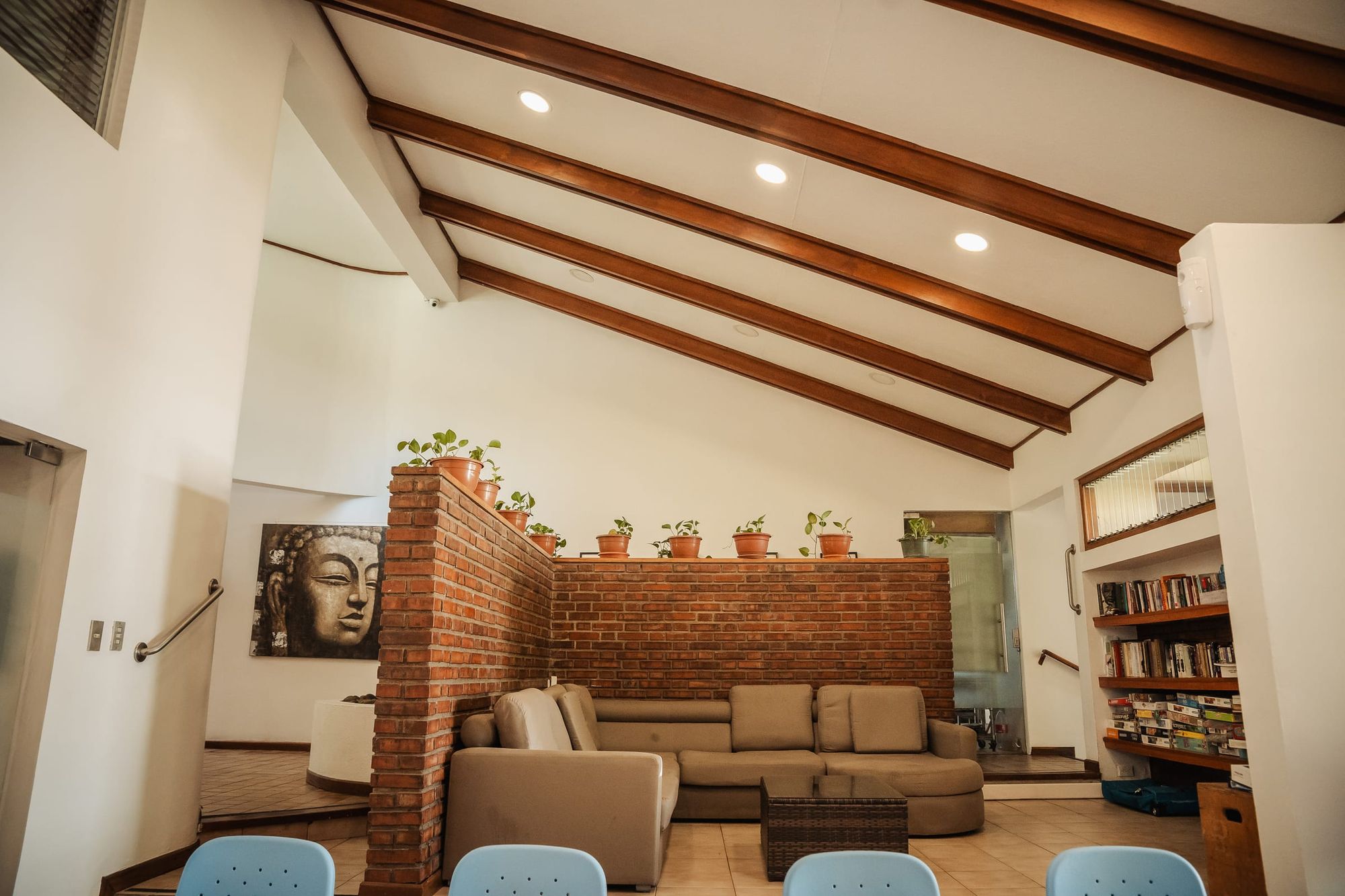 La sala de estar de San José, con un sofá junto a un muro de ladrillo, vigas altas de madera y un librero.