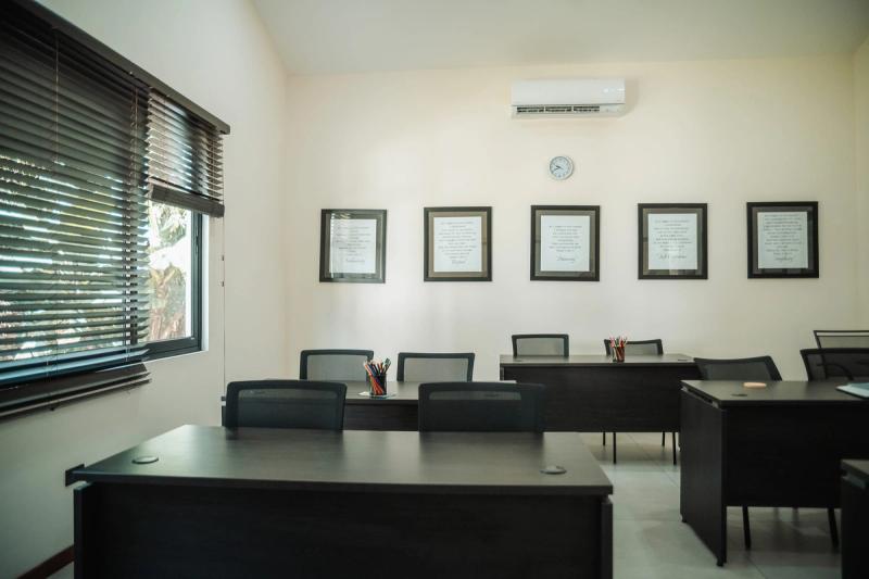 A bright group room at Atenas with dark desks and chairs and a row of framed quotations on the wall.