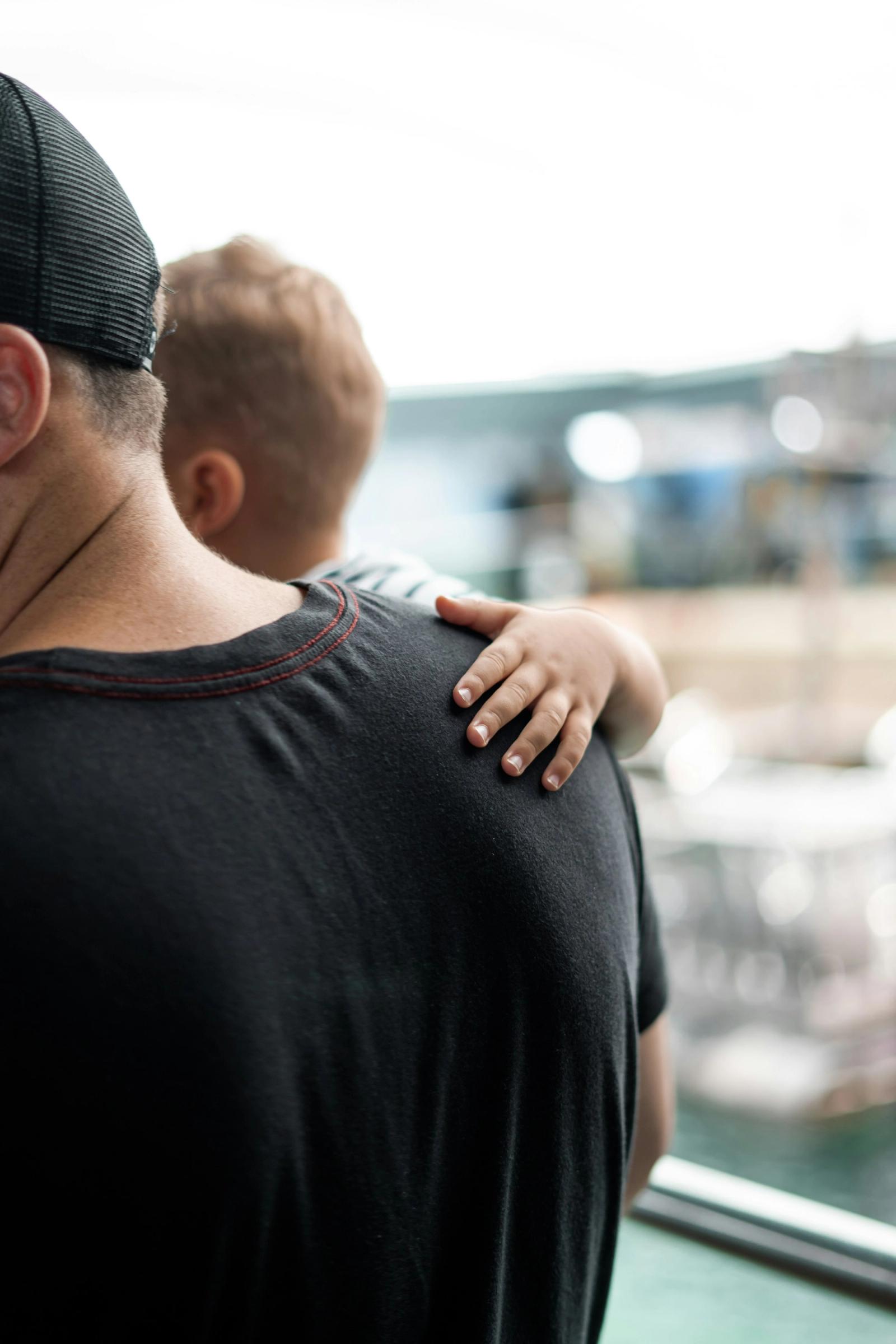 A child's arm resting across an adult's shoulder, seen from behind.