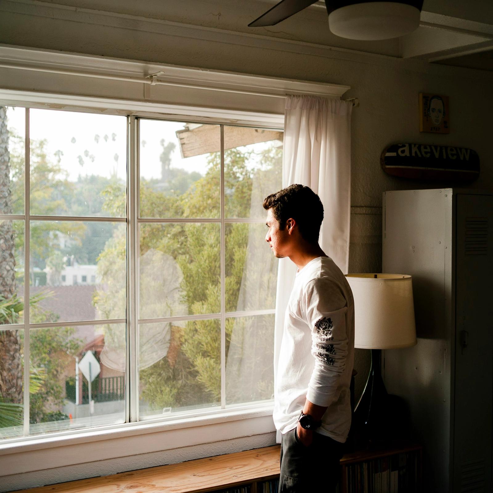 A person standing at a window, looking out in soft daylight.